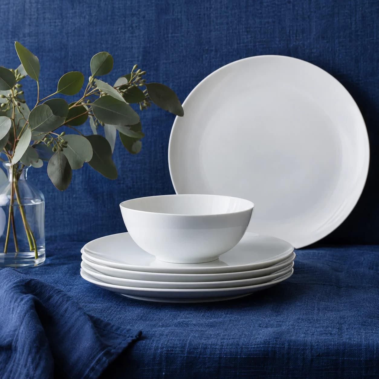 Illustrative thin white dinnerware stacked on cobalt linen